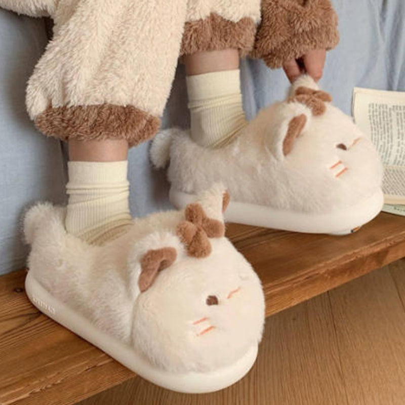 Beige closed-back plush slippers featuring a bow cat design with line eyes and a tiny tail, warm indoor footwear with EVA sole