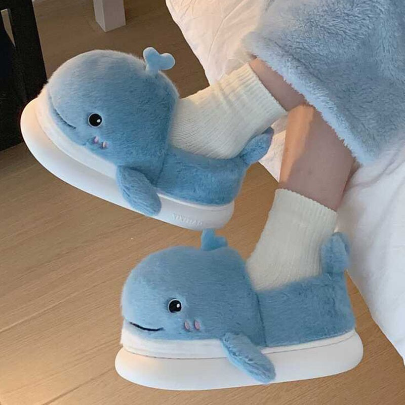 Light blue closed-back plush slippers shaped like a 3D whale with a spout and upturned tail, cozy indoor footwear with EVA sole