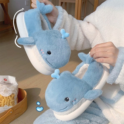 Light blue closed-back plush slippers shaped like a 3D whale with a spout and upturned tail, cozy indoor footwear with EVA sole