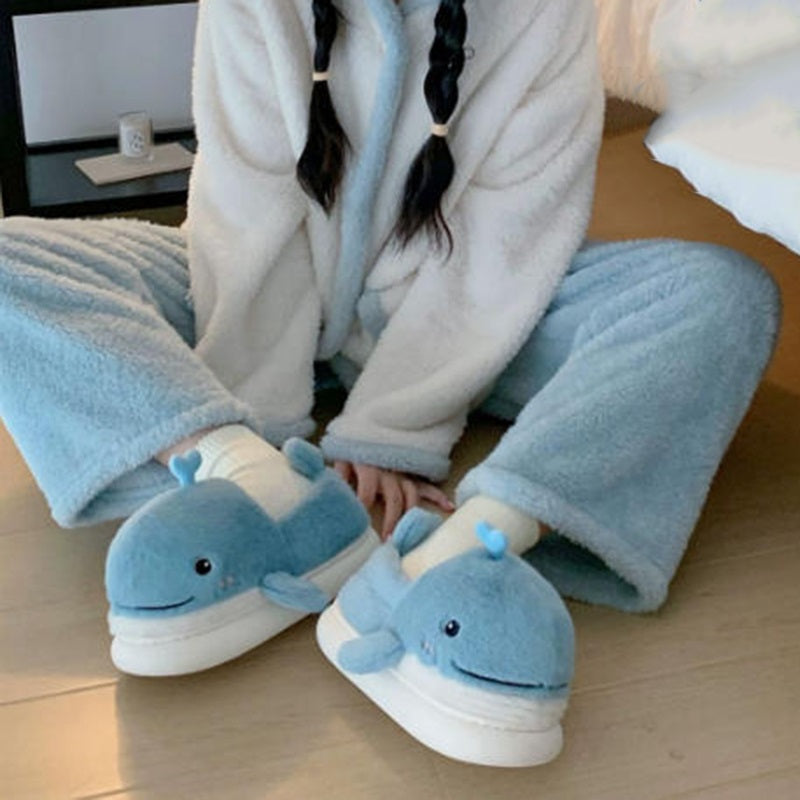 Light blue closed-back plush slippers shaped like a 3D whale with a spout and upturned tail, cozy indoor footwear with EVA sole