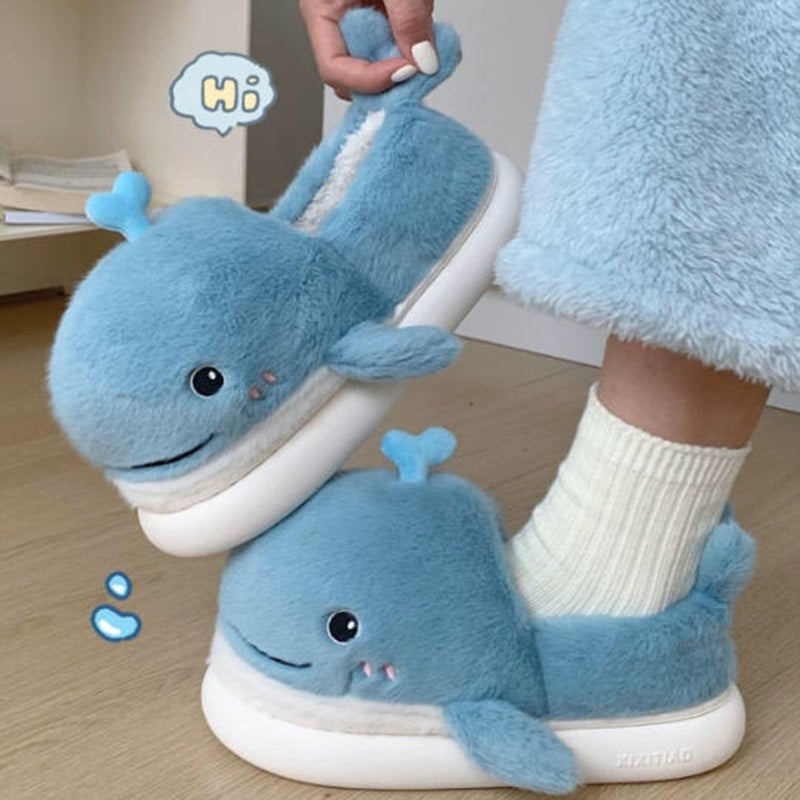 Light blue closed-back plush slippers shaped like a 3D whale with a spout and upturned tail, cozy indoor footwear with EVA sole
