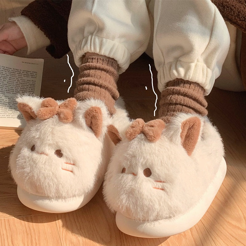 Beige closed-back plush slippers featuring a bow cat design with line eyes and a tiny tail, warm indoor footwear with EVA sole